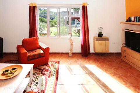Salón luminoso con sillón rojo y puerta al jardín – Chio, Tenerife