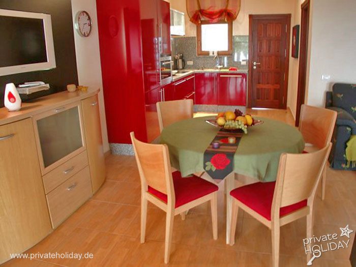 Dining area with round table and red kitchen – Guía de Isora, Tenerife