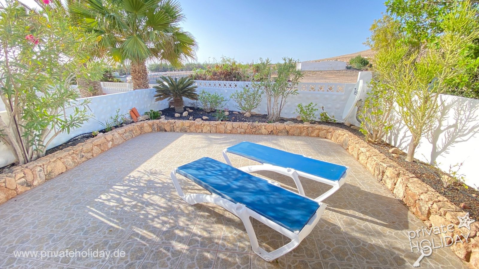 Terrasse ensoleillée avec deux chaises longues et bordure en pierre – Costa Calma, Fuerteventura